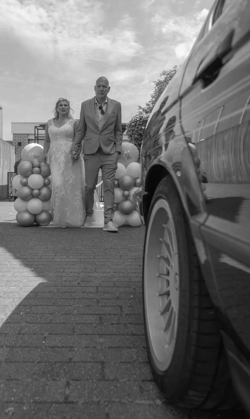Bruidspaar loopt naar de trouwauto, trouwfotografie in zwart-wit
